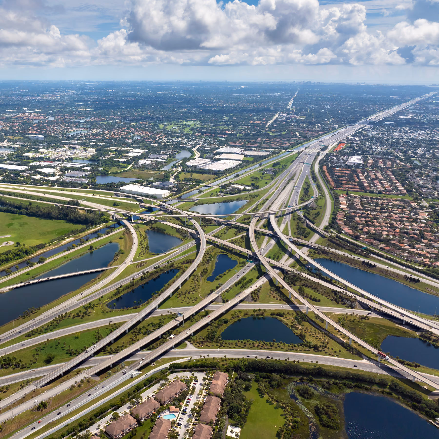 Aerial view of a large highway interchange surrounded by water, greenery, and residential areas.