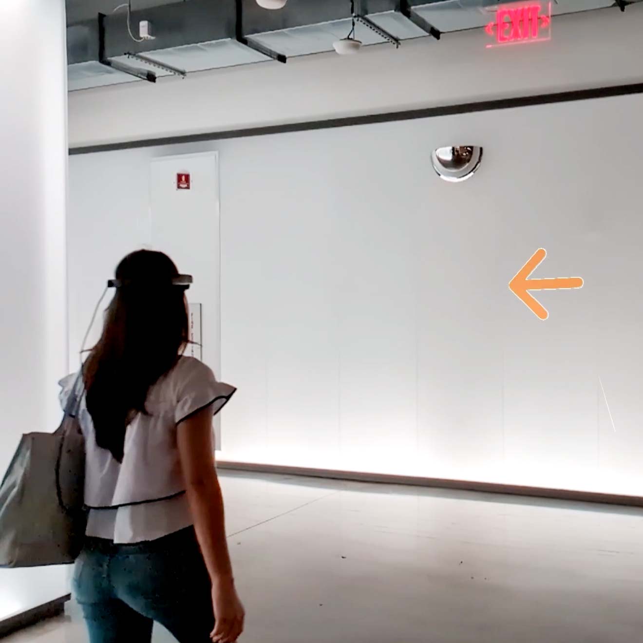 A woman walking down a hallway wearing an AR device, following digital navigation arrows.