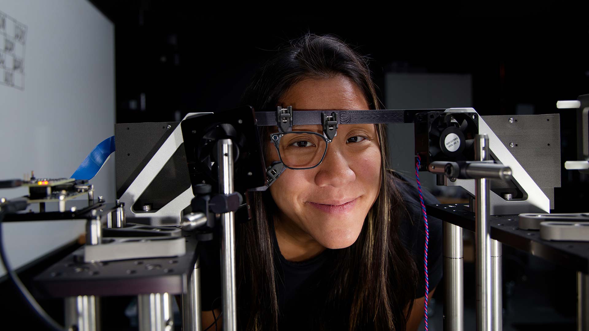 A woman looks through a waveguide held in testing frame within a laboratory.