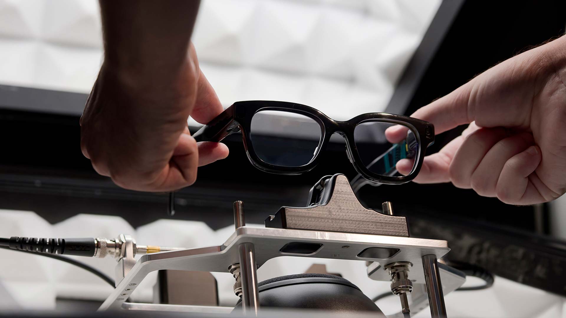 Two hands gently place an AR glasses prototype onto a base for testing and evaluation.