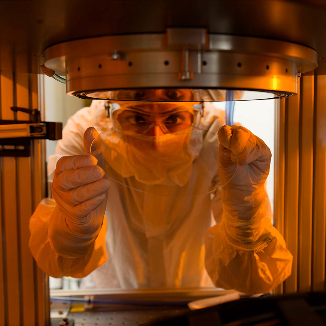 A Magic Leap engineer wearing personal protective gear makes adjustments to custom machinery for waveguide materials production.