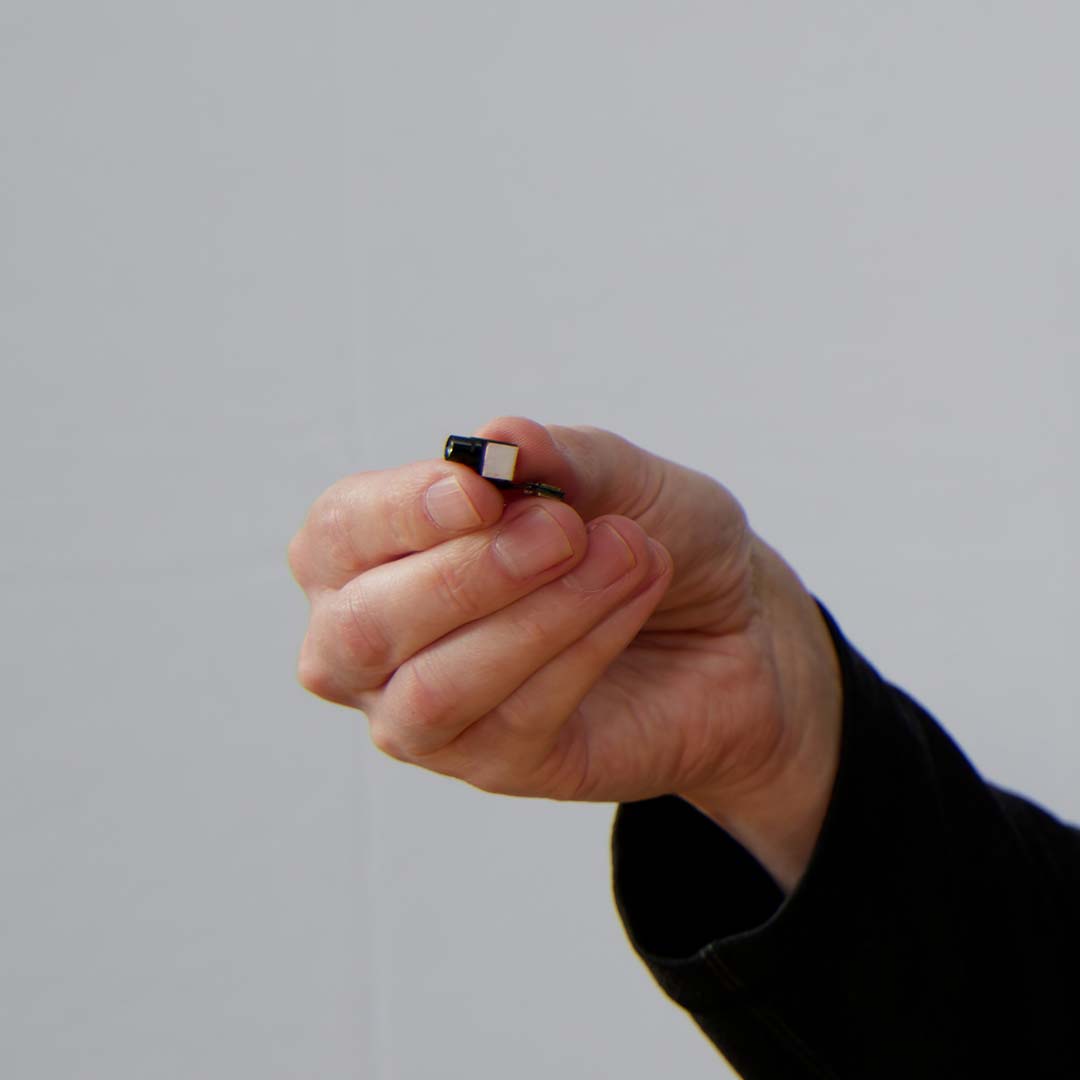 A hand holds a small  MicroLED projector, which is implanted in the AR glasses frame.