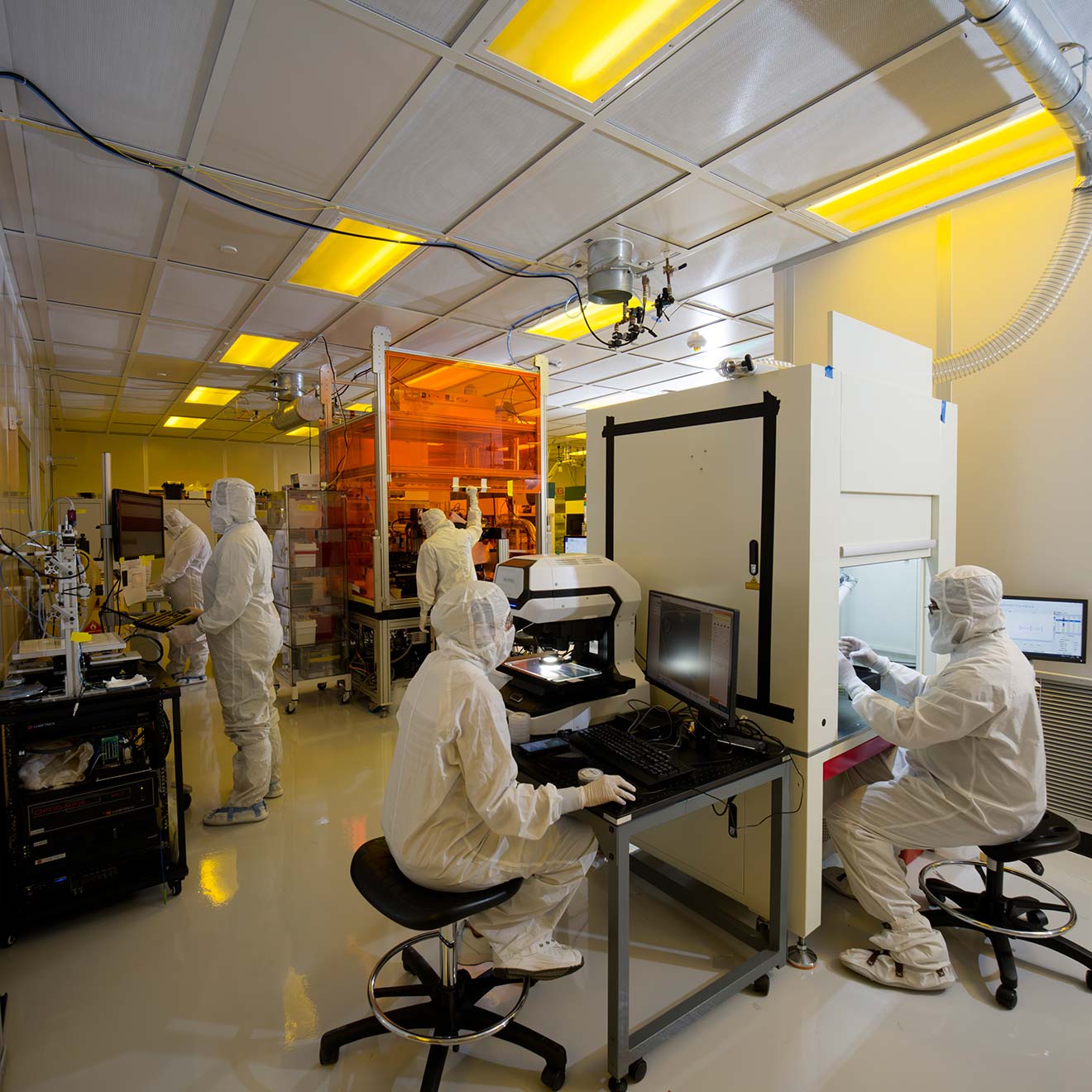 A group of Magic Leap engineers collaborating at adjacent workstations in a manufacturing clean room.