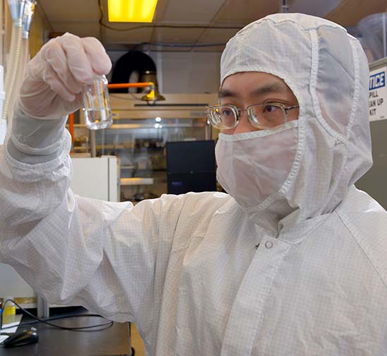 A Magic Leap chemist wearing a clean room bunny suit and goggles holds up a vial of liquid inside a clean room laboratory.