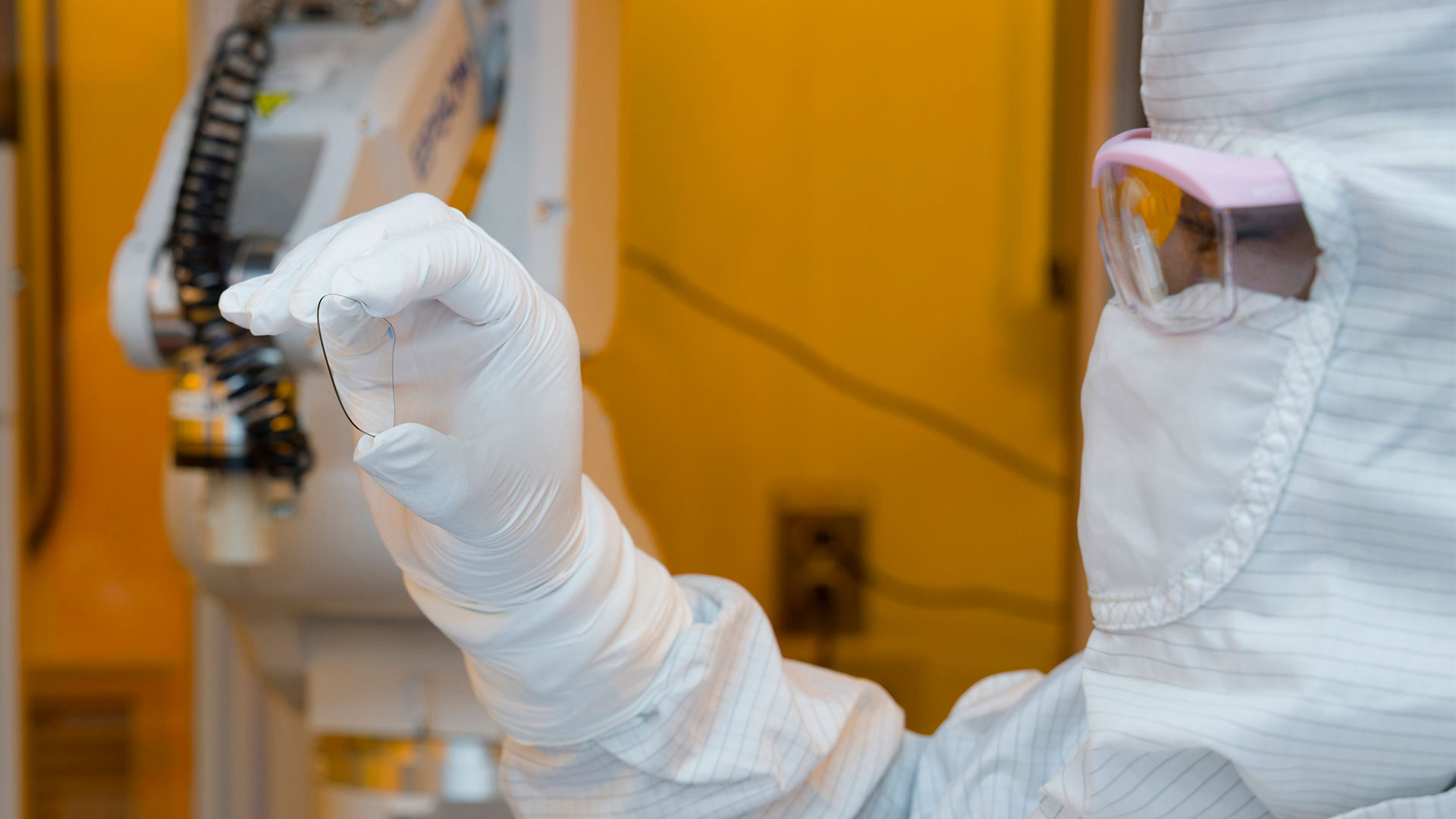 A gloved hand holds a Magic Leap waveguide, with lab machinery in the background.