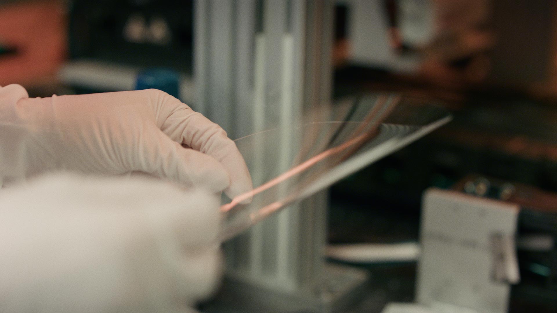 Gloved hands bend flexible wafer materials.