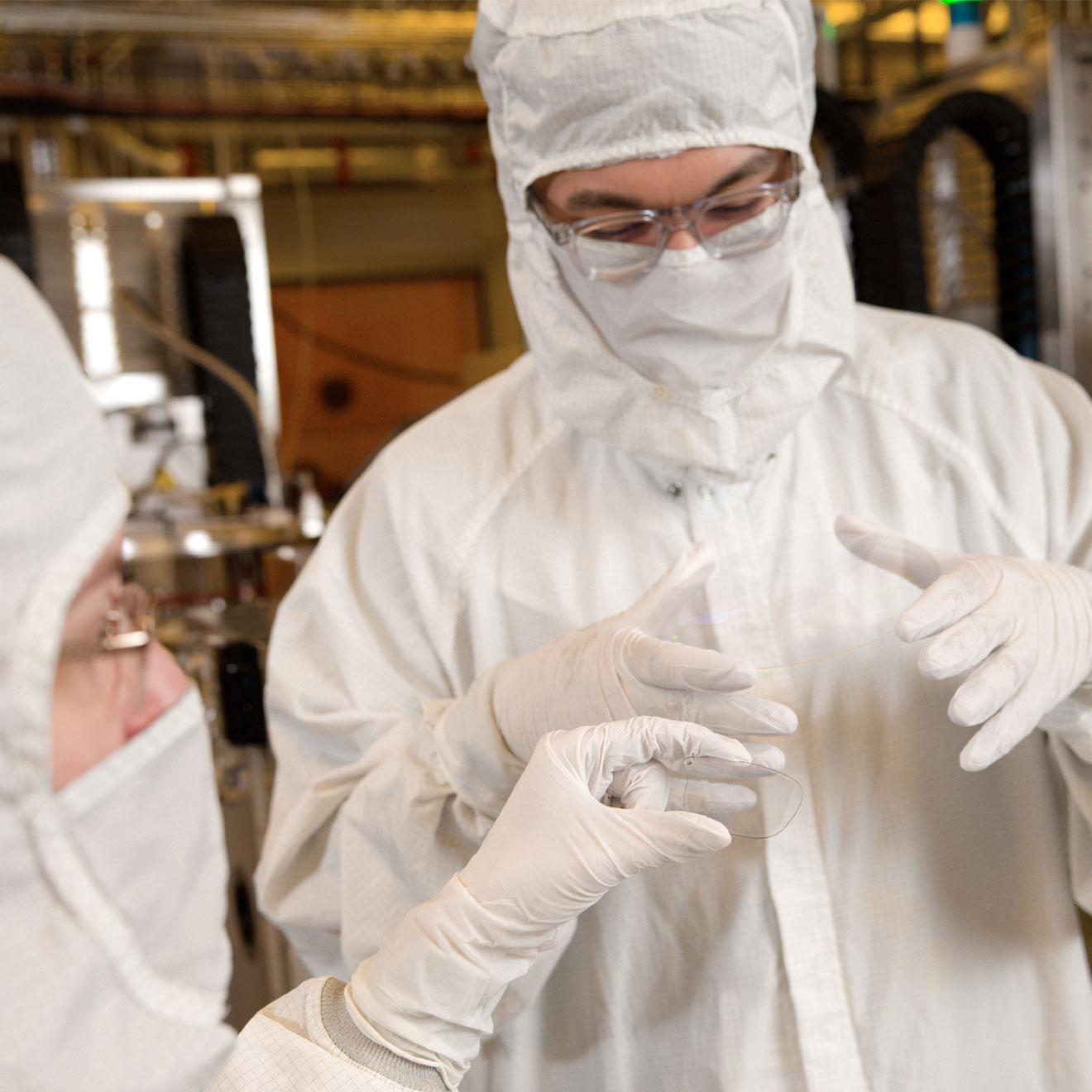 In one of Magic Leap's production facilities, a technician in a clean room bunny suit carefully holds an uncut waveguide wafer.