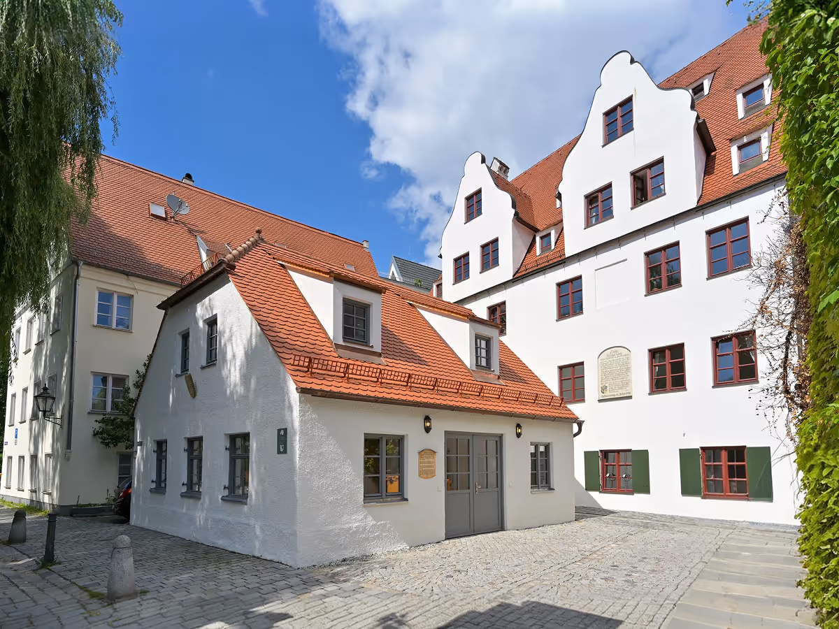 Historische weiße Gebäude mit roten Ziegeldächern und Kopfwandgiebeln an einem sonnigen Tag mit blauem Himmel.