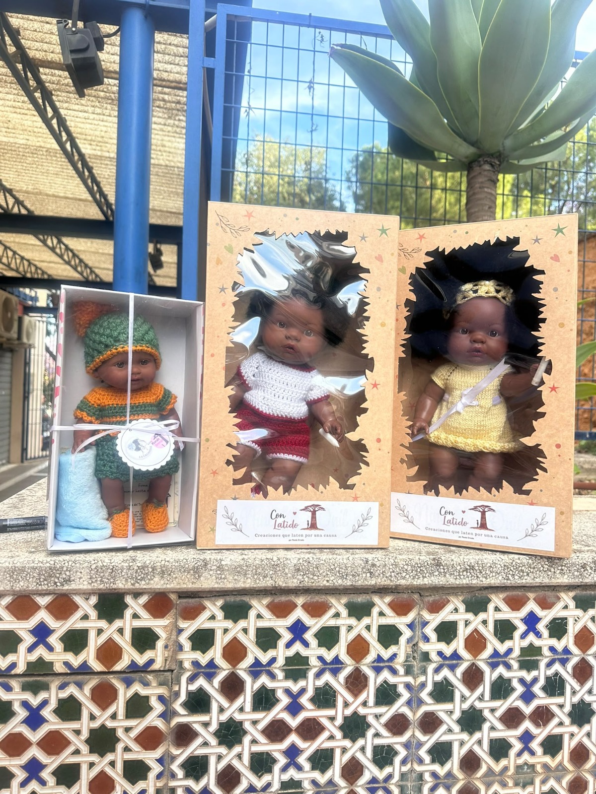 Muñecas solidarias de Mundo Orenda en sus cajas, sobre un banco de azulejos
