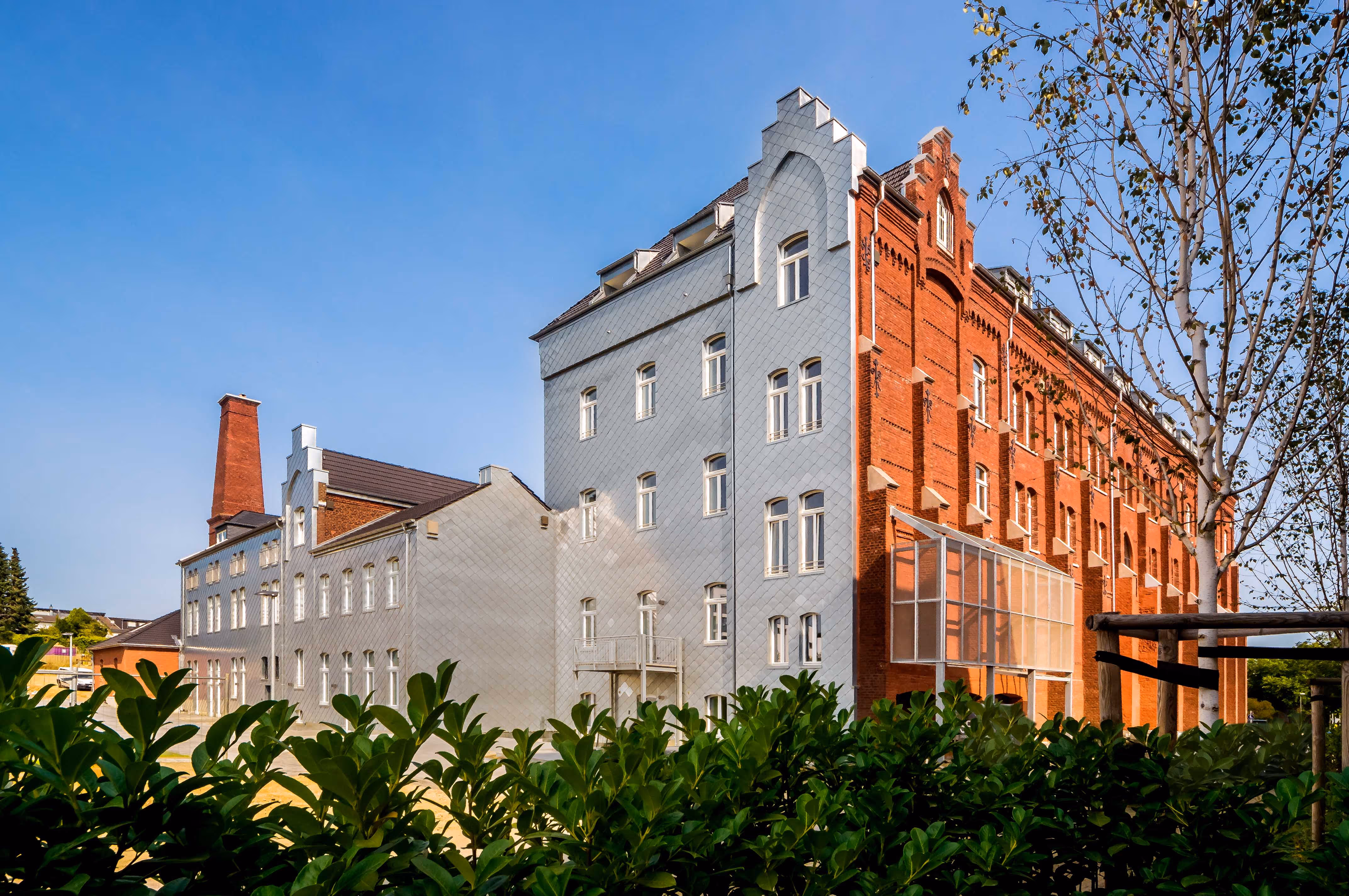 Historisches Gebäude mit einem Teil in rotem Backstein und einem Teil mit grauer Fassade unter blauem Himmel.
