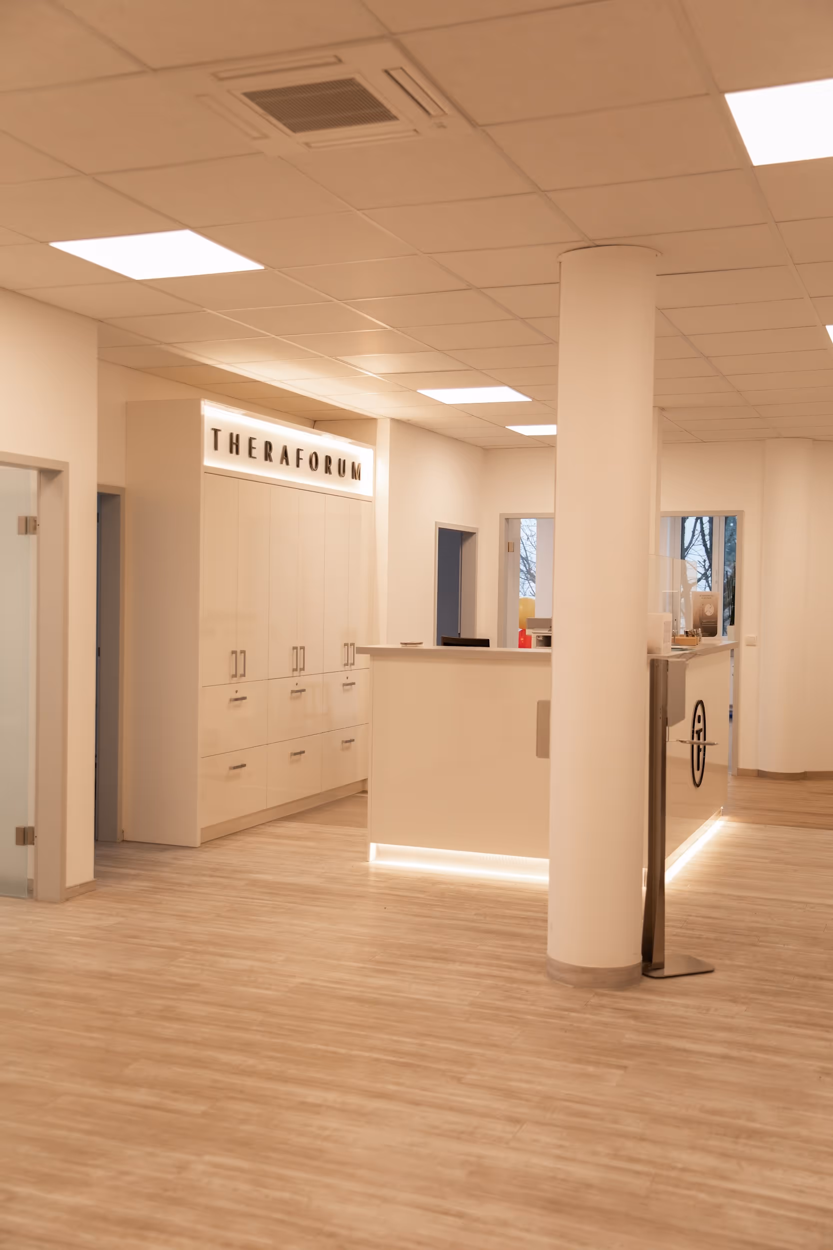 Moderner Empfangsbereich mit heller Beleuchtung, weißem Empfangstresen, und Wandschrank mit Aufschrift 'Theraforum'.