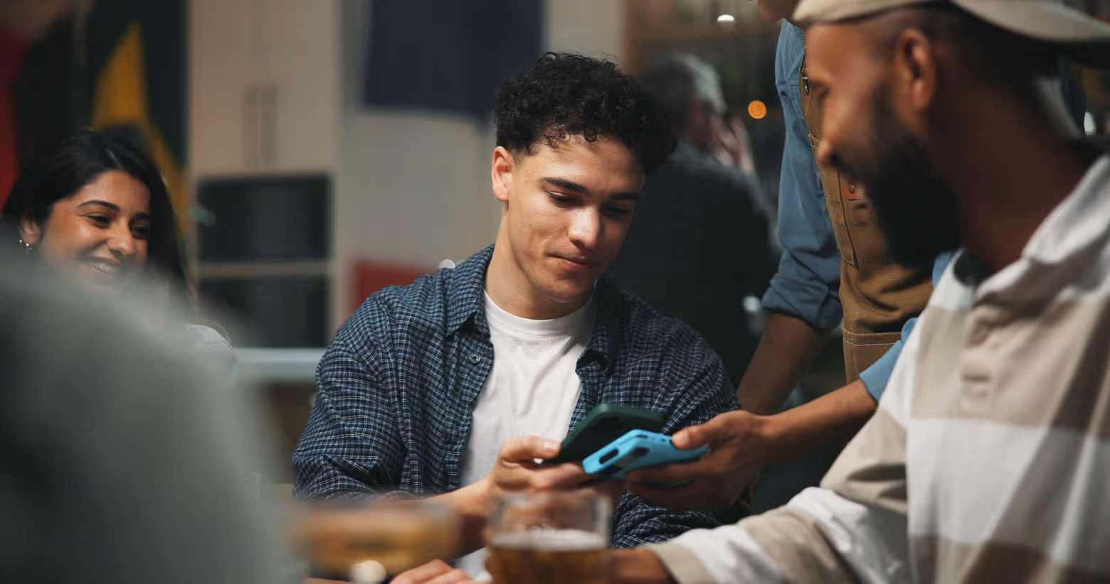 Young people sharing and looking at smartphones together in a casual social setting.