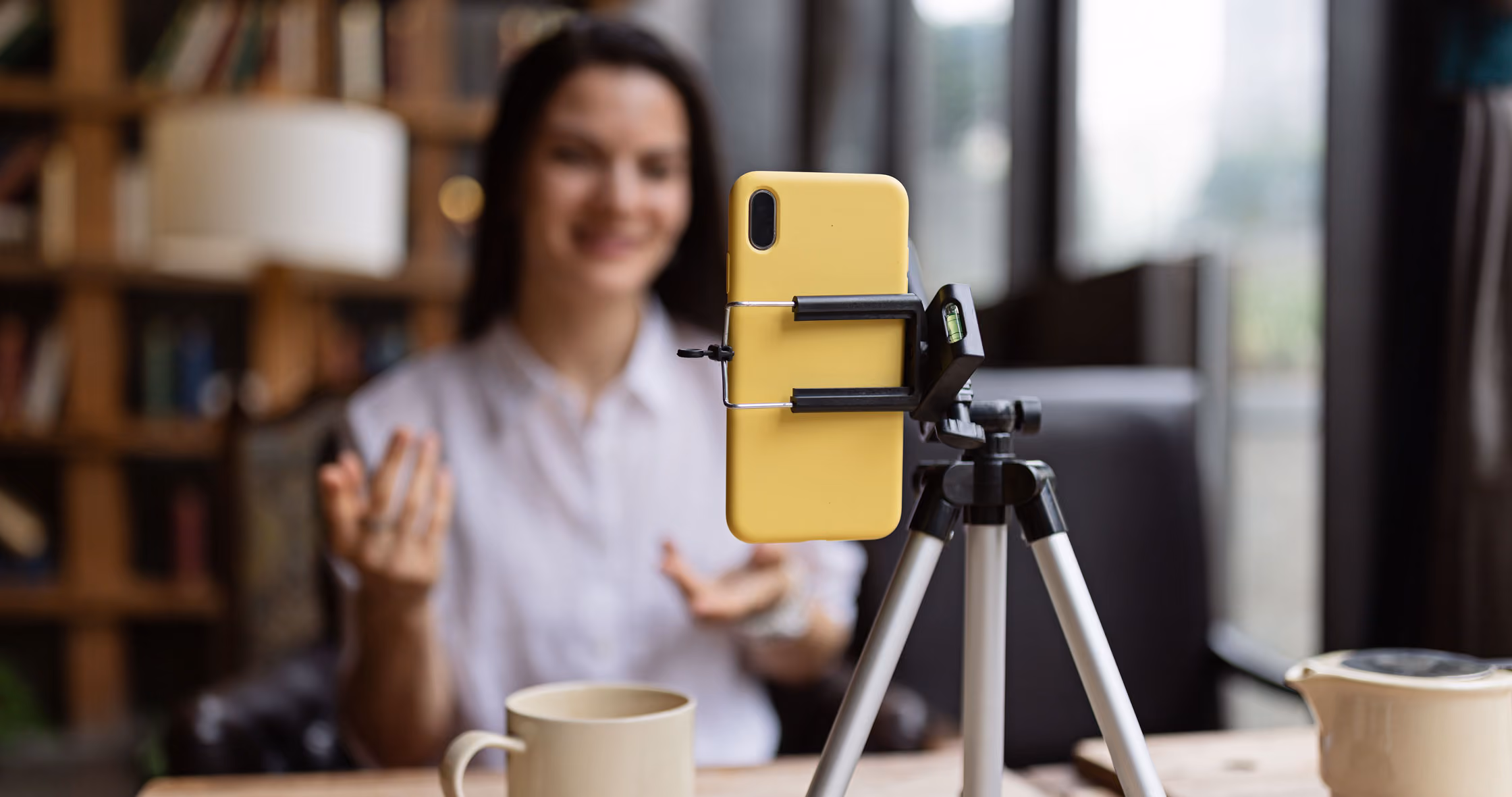Woman recording video on smartphone mounted on a tripod in a cozy room.