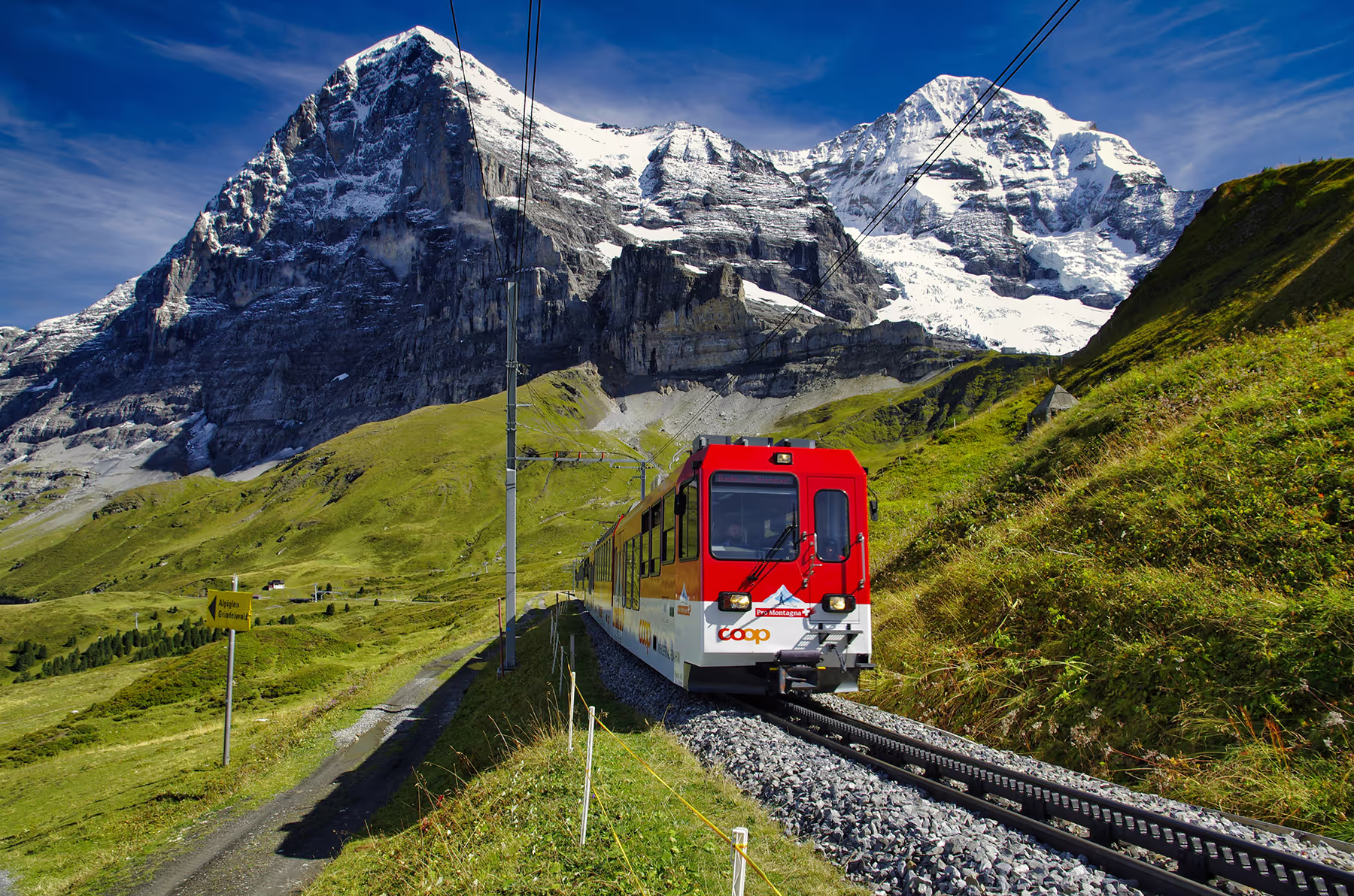 A scenic view of a train traveling through the Swiss mountains, surrounded by lush green valleys and towering peaks