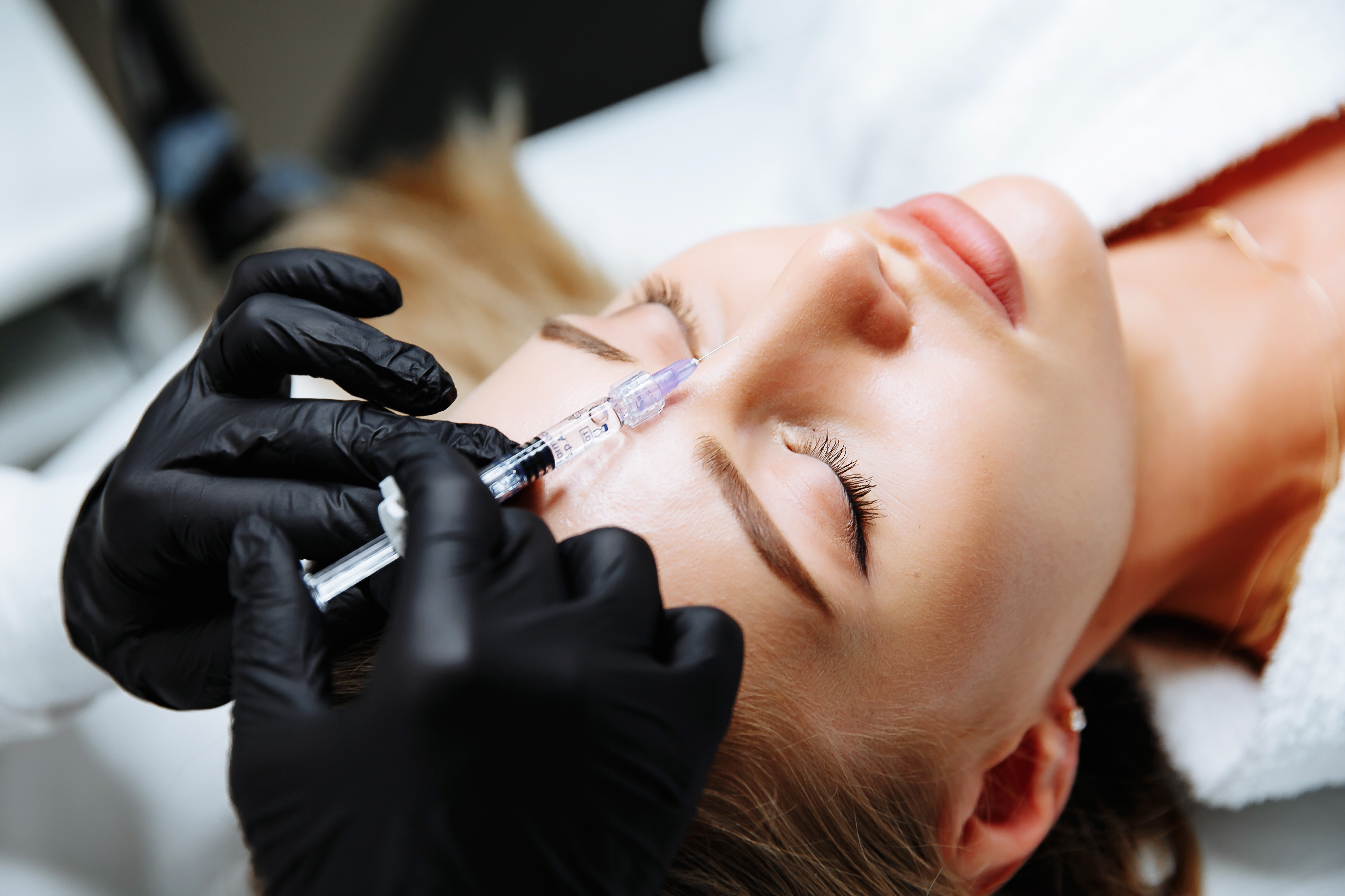 Gloved hands performing an injectable treatment on a patient's brow