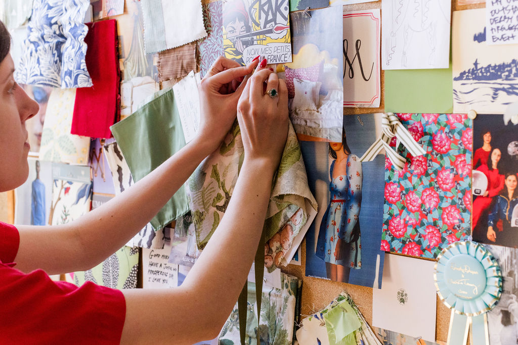 Person pinning fabric samples and fashion sketches to a bulletin board with various colorful textile swatches and drawings.