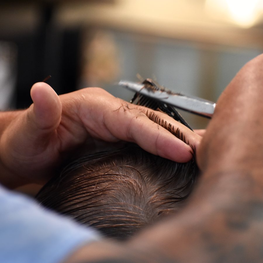 Close-up of a barber cutting hair using scissors and a comb.