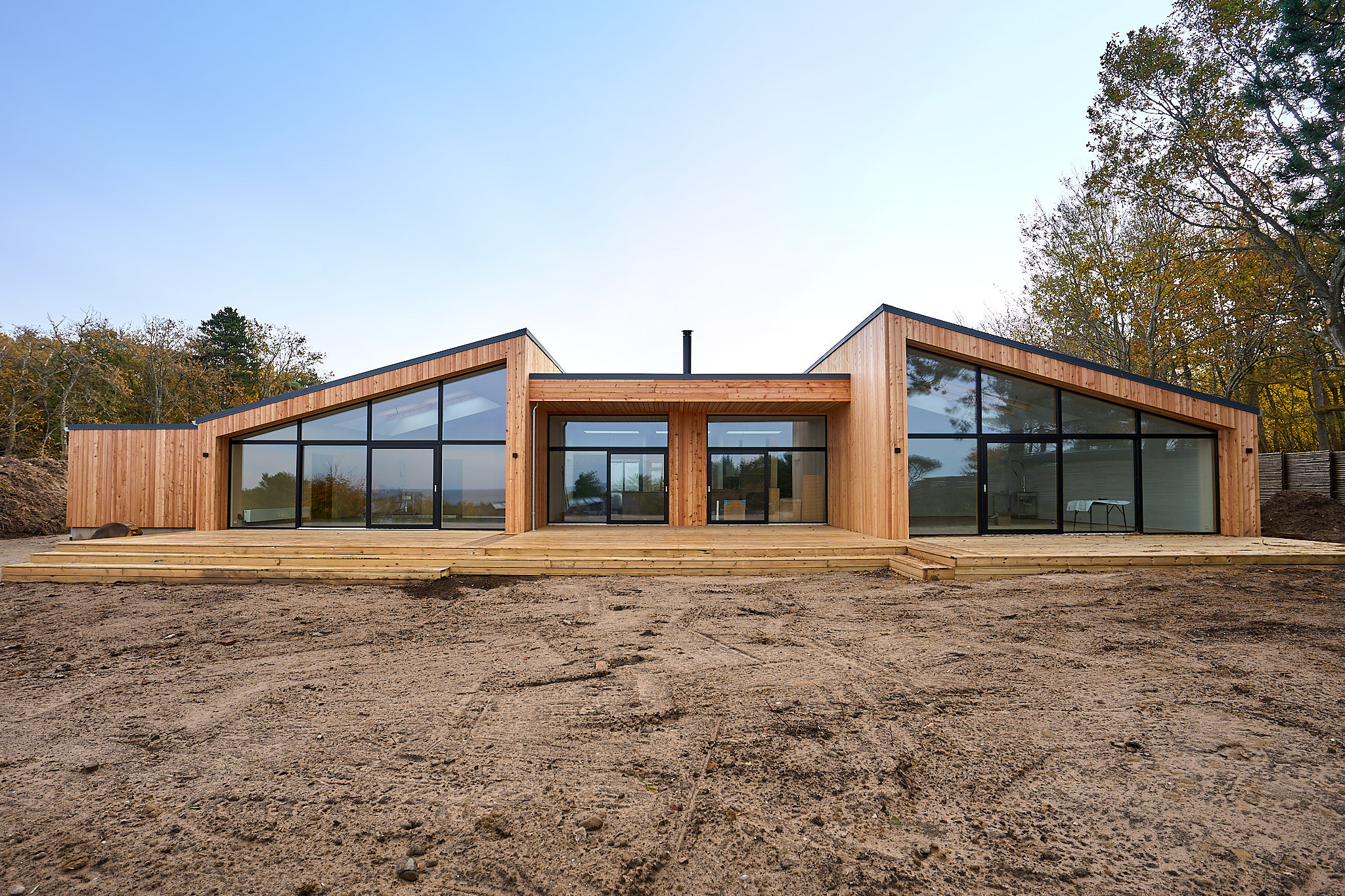 Modern wooden house with large floor-to-ceiling windows and slanted roofs surrounded by trees.