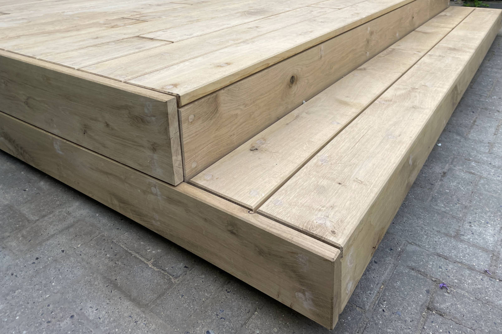 Close-up of a corner of a wooden outdoor terrace with light wood planks and visible grain patterns.