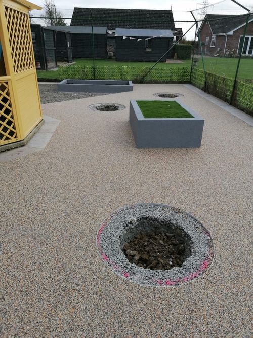 Resin bound aggregate flooring inside cat enclosure. Three circular holes have been dug out the flooring and filled with top soil ready for shrubs and small plants to be plated. There is also a raised bed with green turf where the cats can lounge on.