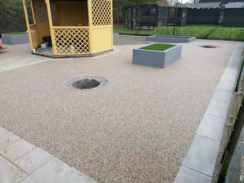 Cat enclosure showing the new resin bound aggregate flooring surrounding the wooden shed in the middle. Running the perimeter of the enclosure is a slabbed path visitors can use to walk around the enclosure.