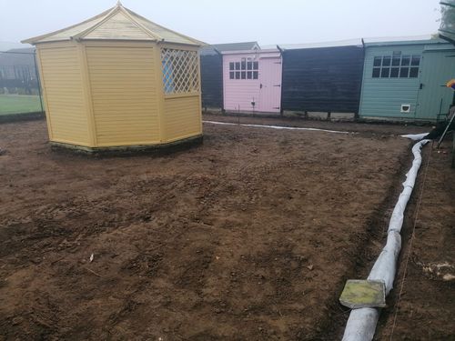 Image showcasing the cat enclosure under revamp. The lawn has been ripped up around the gazebo ready for new flooring to be laid. A small ditch has been dug out around the perimeter with piping fitted for land drains to help drain excess water so flooding does not occur.