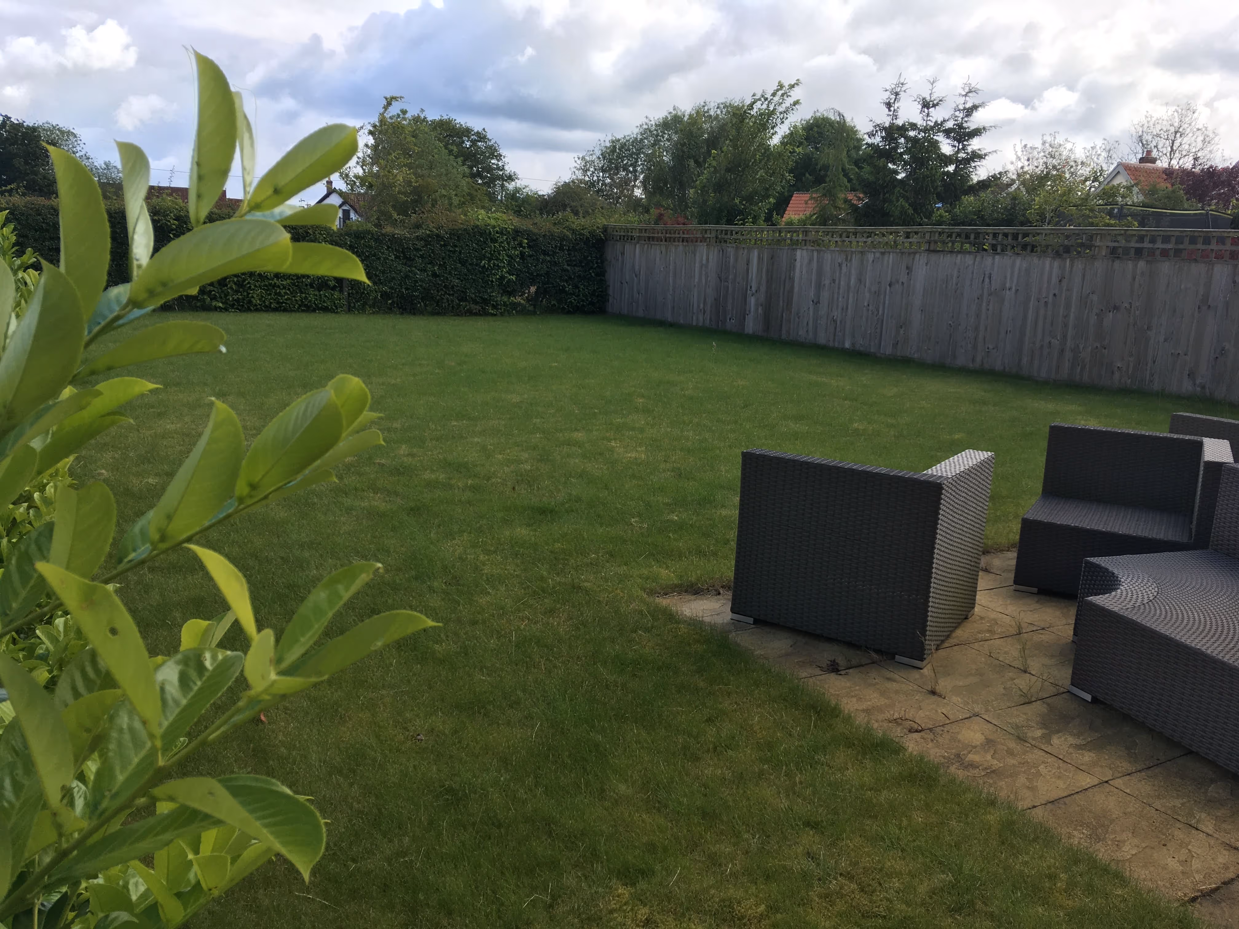 Boring plain back garden with hedge at the bottom and old wooden fence along the side.