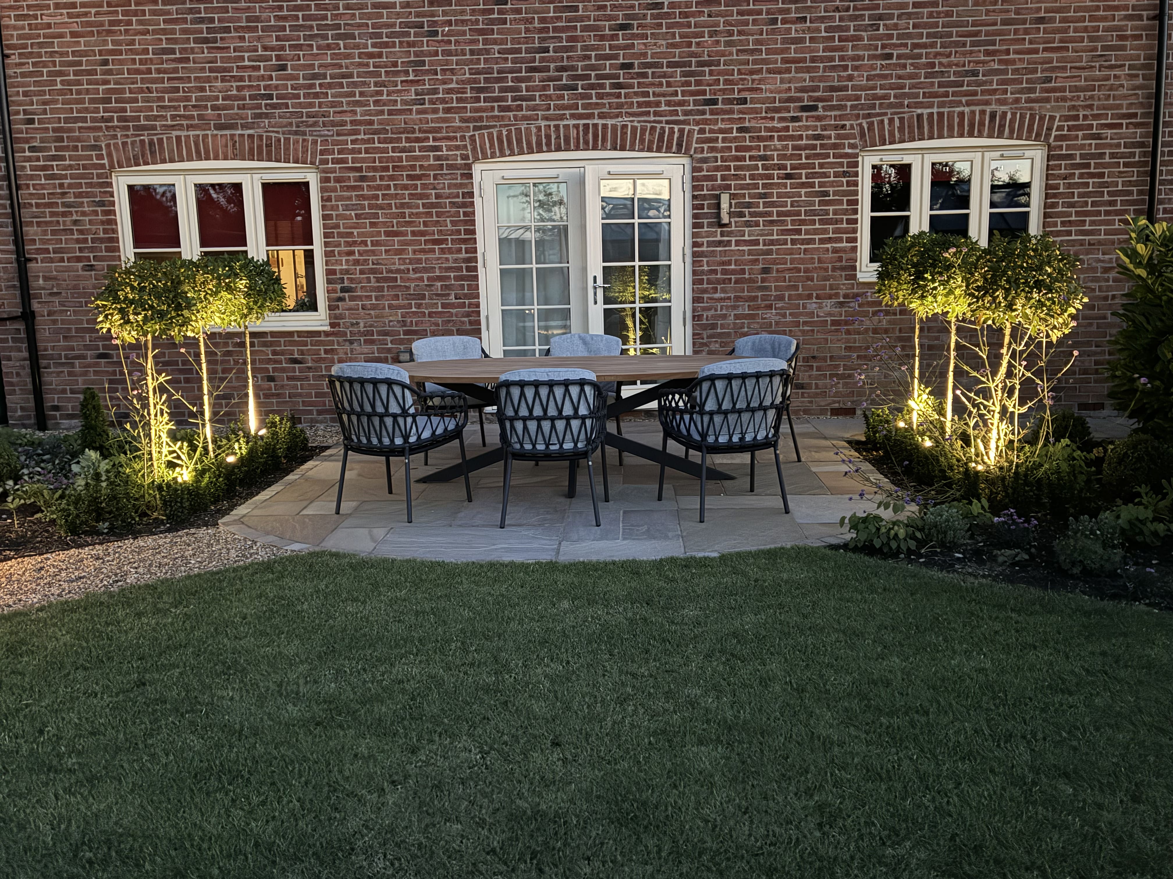 Outdoor dining area with lit dwarf trees either side of the dining area creating a very relaxed secluded atmosphere just outside french doors at the rear of the house.