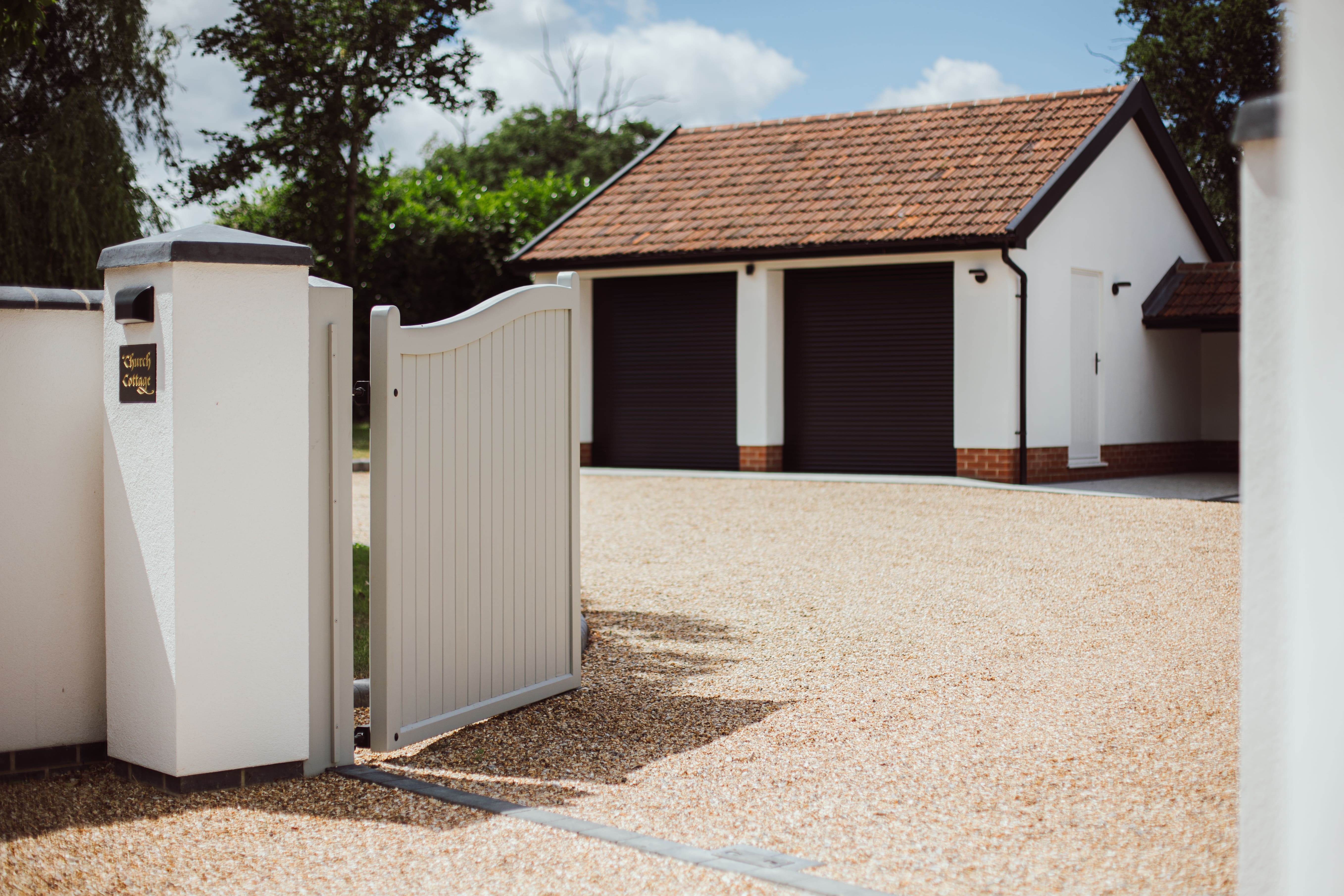 Front View of a Gravel Driveway and gates, background you can see a two door garage