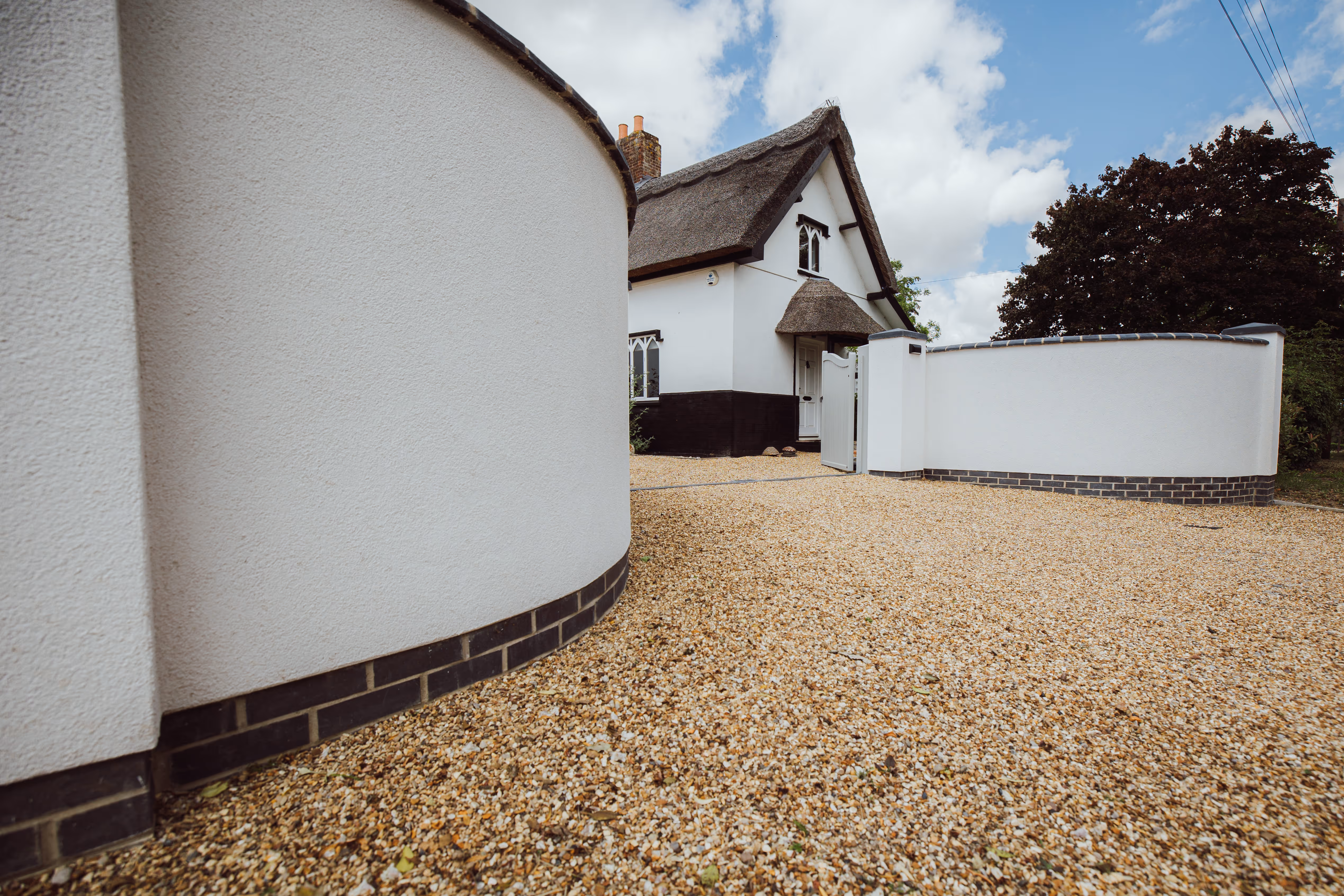 Curved white rendered walls and Church Cottage leading around a gravel driveway.
