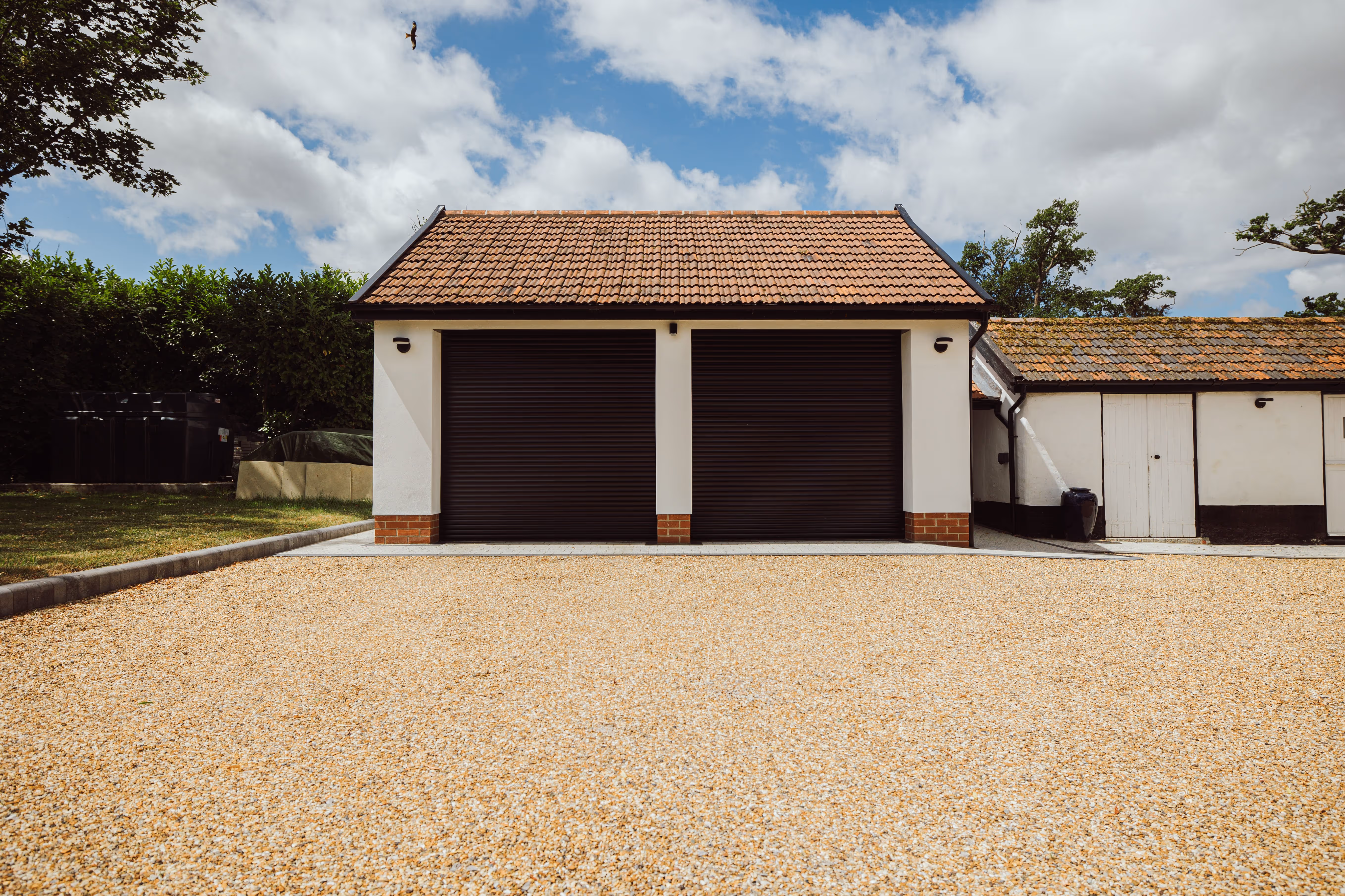 Front view of double garage doors, white rendered walls and gravel driveway. 