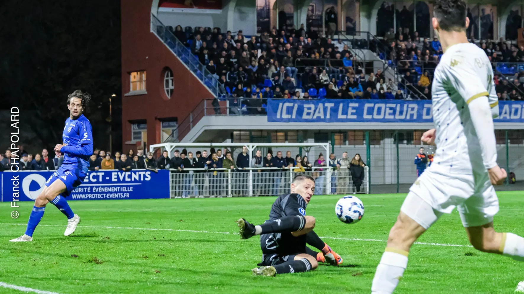 Match de football intense avec un gardien en action et des spectateurs.