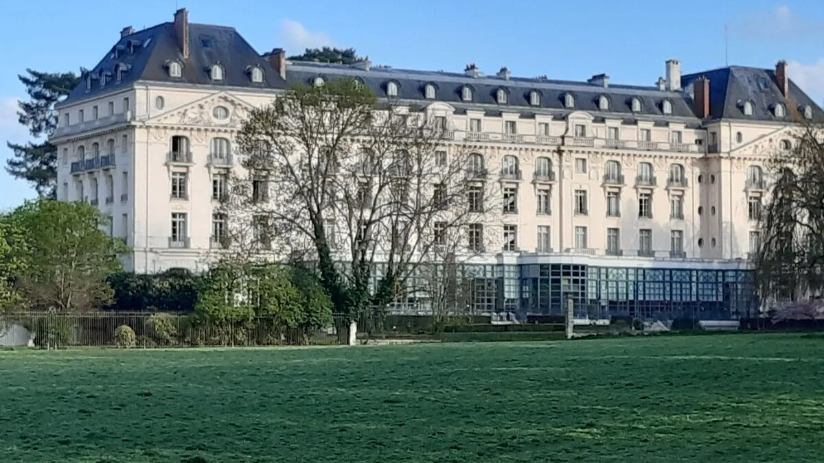 Bâtiment historique avec jardin verdoyant et ciel ensoleillé.