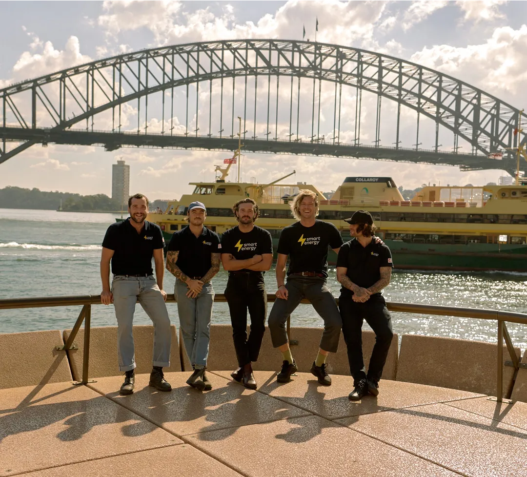 Five Smart Energy team members in company shirts pose on a waterfront promenade with ferries and a bridge in the background.