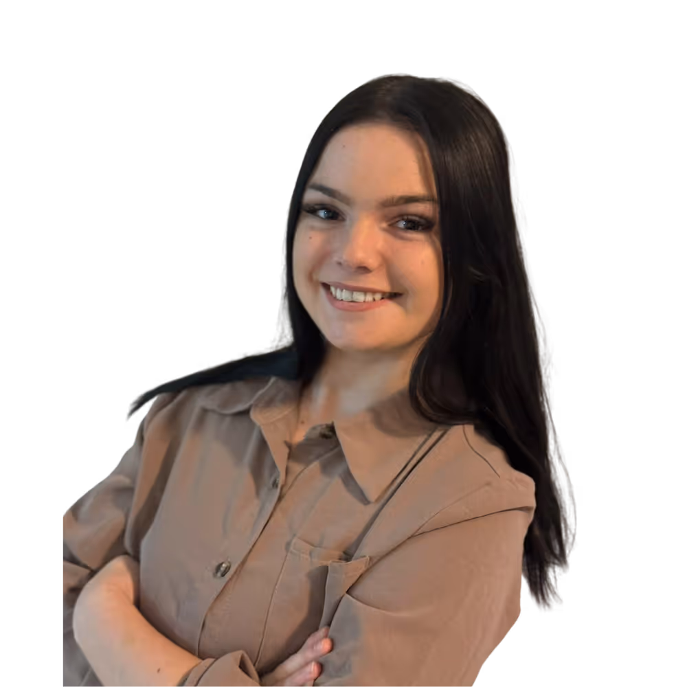 Junge Frau mit langen dunklen Haaren lächelt mit verschränkten Armen und trägt eine beigefarbene Bluse.