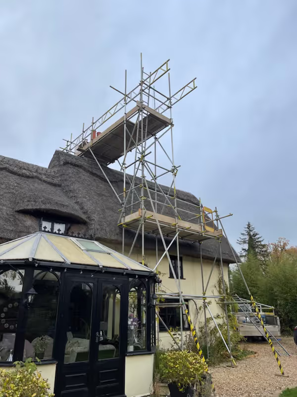 Scaffolding along the front a house with a thatched roof viewed from the left.