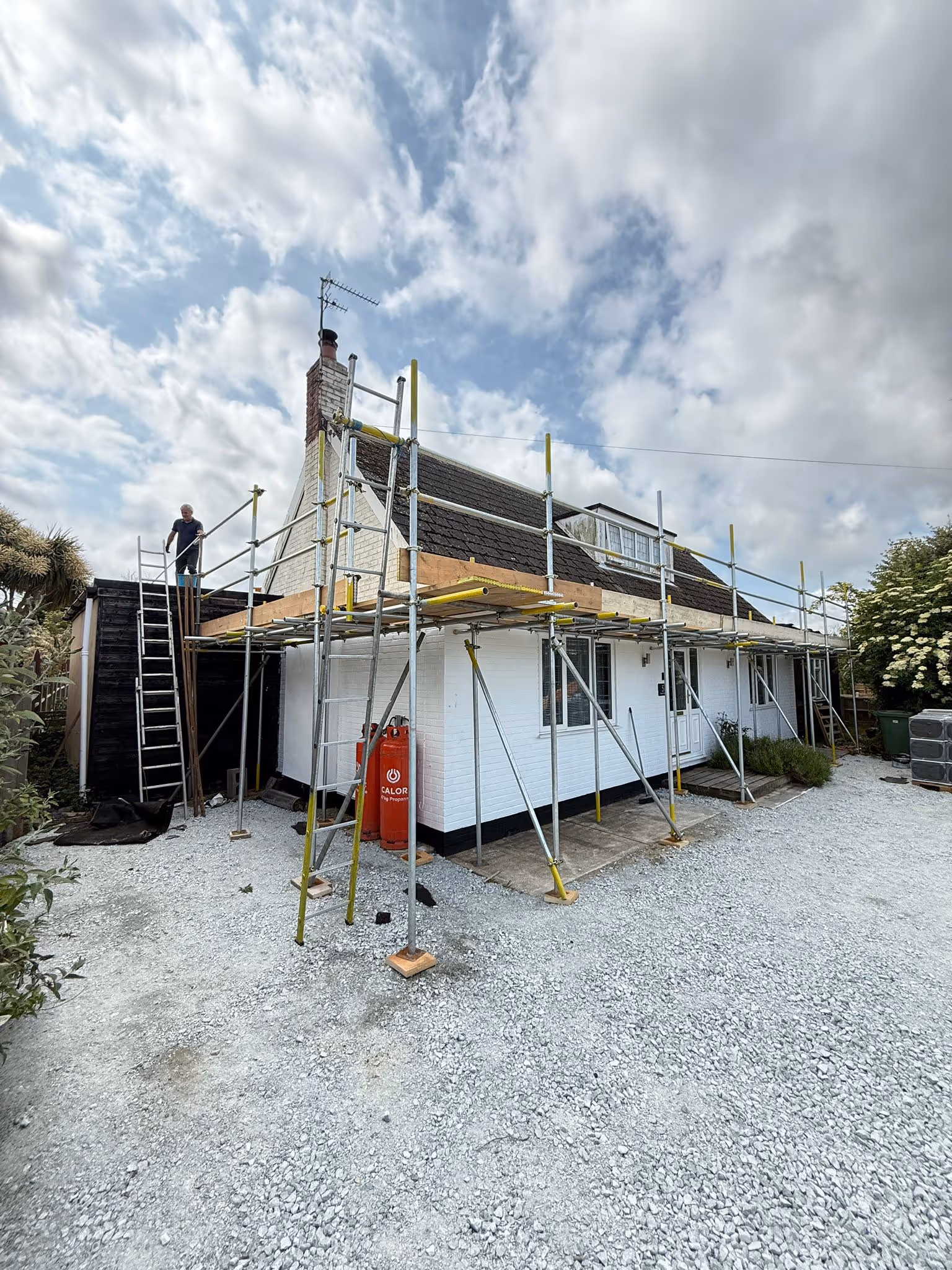 Scaffolding along the front and side of white bungalow with workmen on the platform.