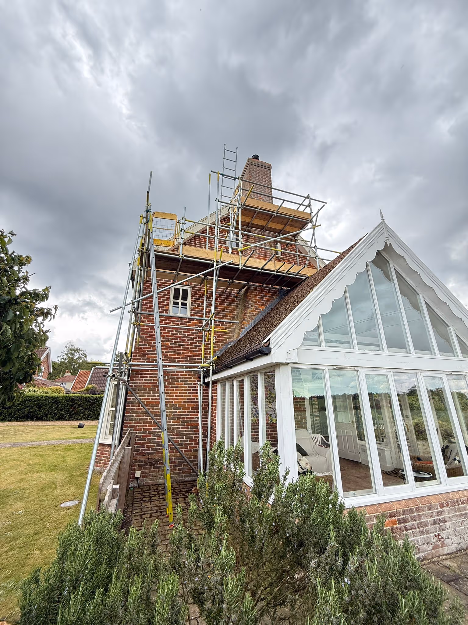 Scaffolding assembled along brick wall next to conservatory to allow access for work to be done on chimney.