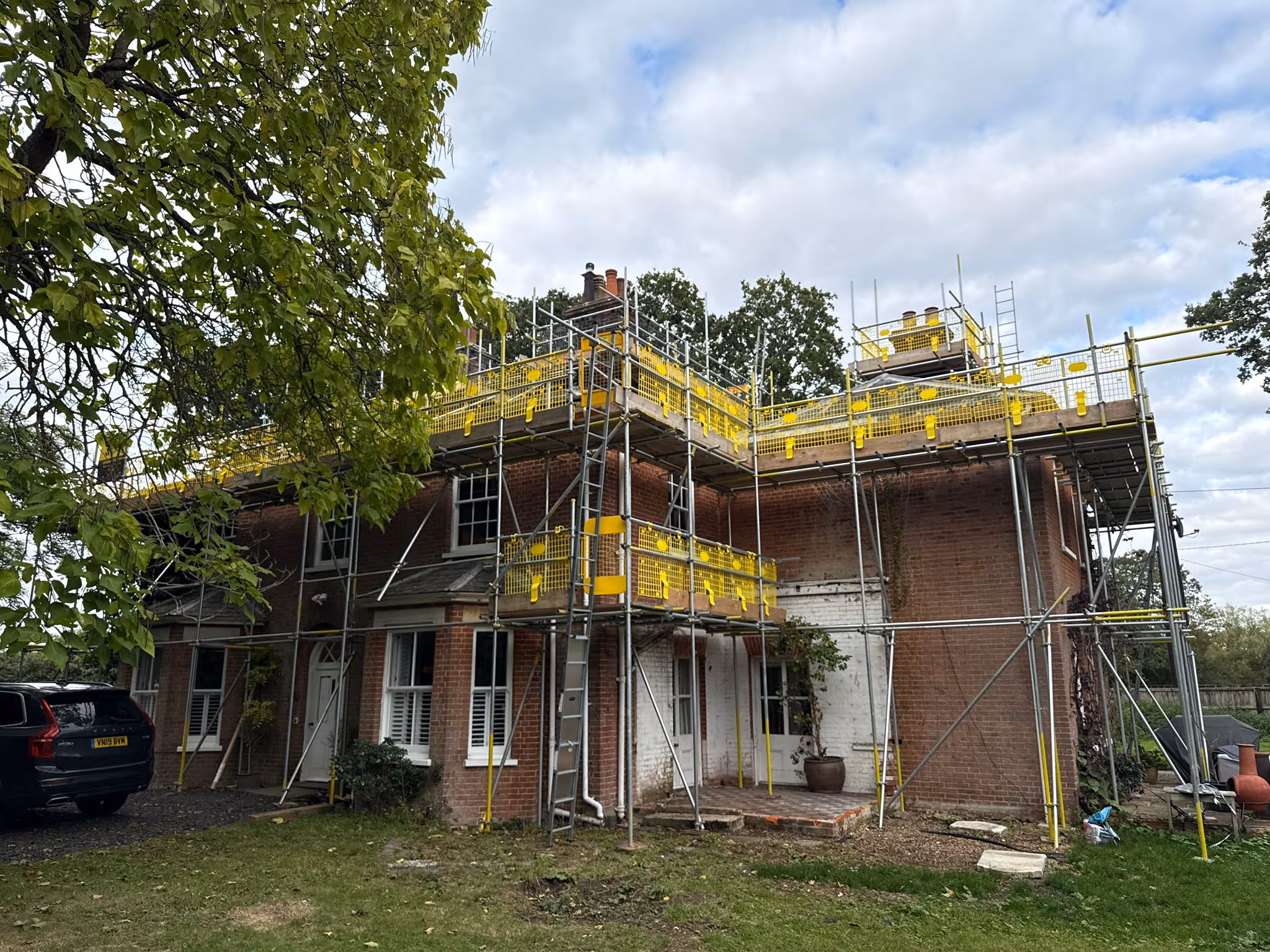Scaffolding constructed around brick house. The scaffolding structure has alowed opportunity for work to be done on roof and chimney tower.