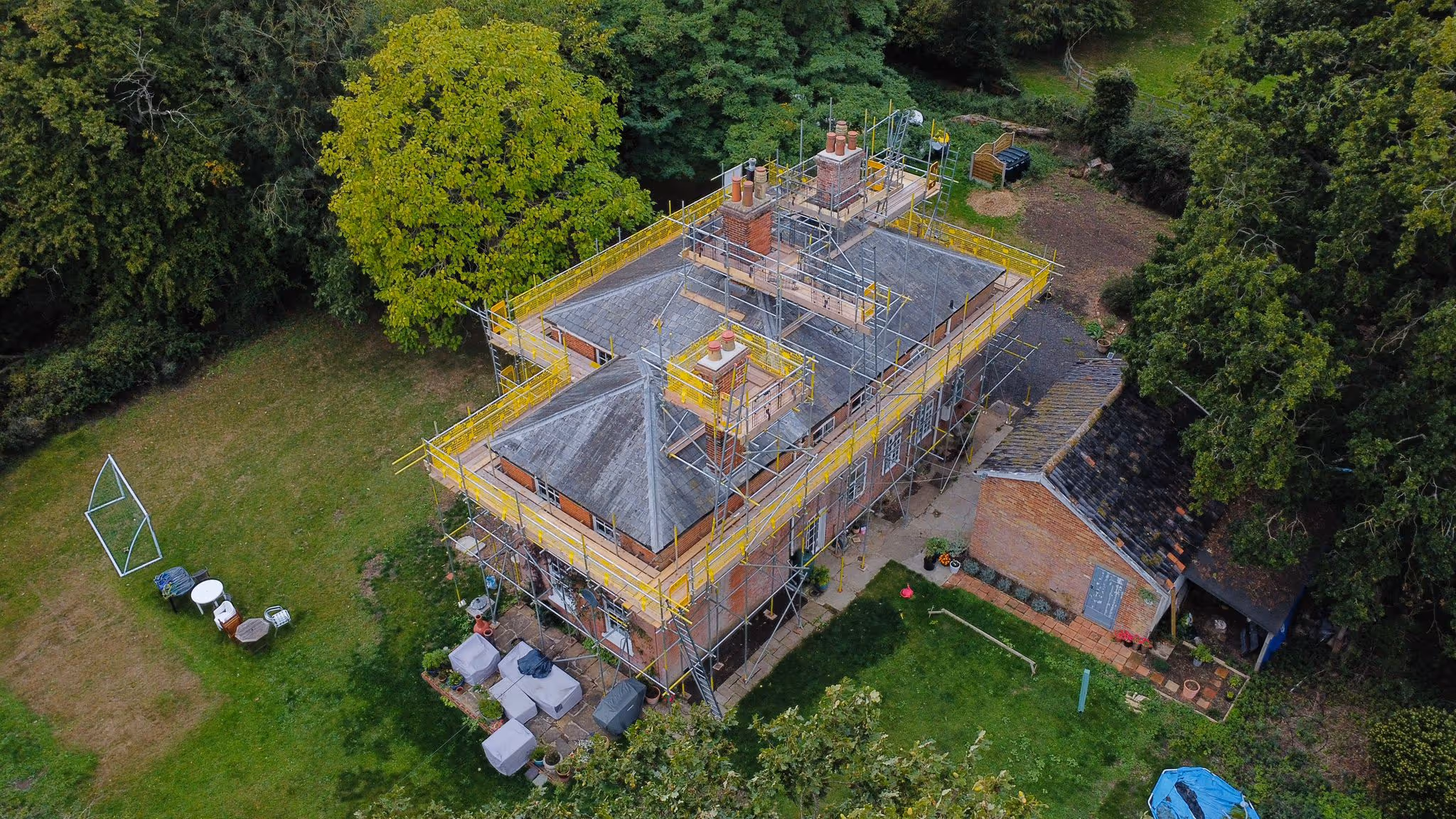 Photo taken from birds eye view of house showcasing scaffolding structure built around the perimeter of the building. Wooden plank walkway also around the perimeter of the building.