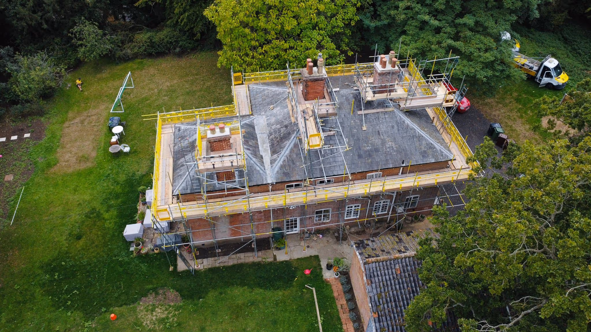Photo taken from birds eye view of house showcasing scaffolding structure built around the perimeter of the building. Wooden plank walkway also around the perimeter of the building.