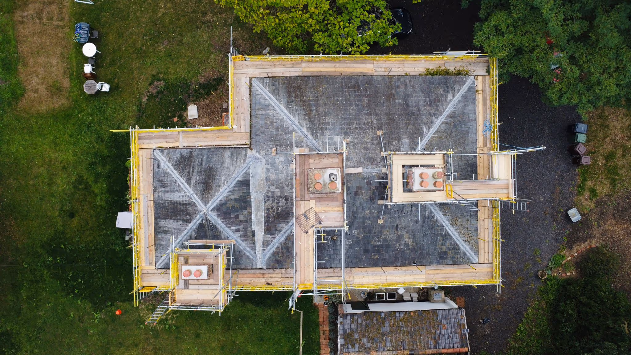 Photo taken from birds eye view of house showcasing scaffolding structure built around the perimeter of the building. Wooden plank walkway also around the perimeter of the building.