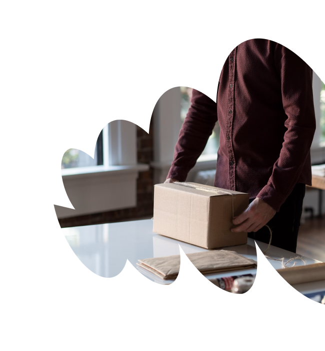 A person holding a cardboard package on a table with mail supplies