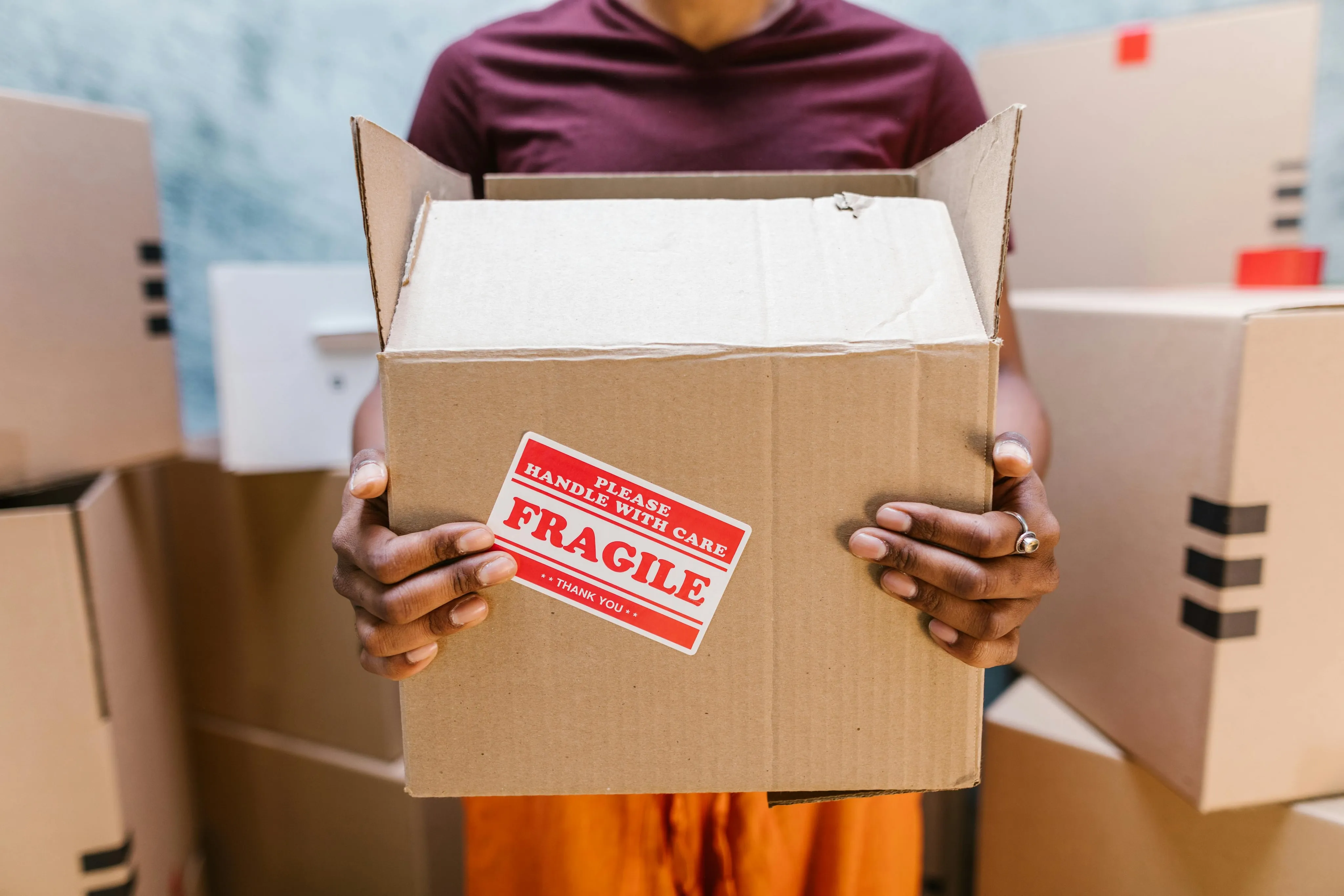 A person holding a cardboard box labeled "Fragile: Please Handle with Care."