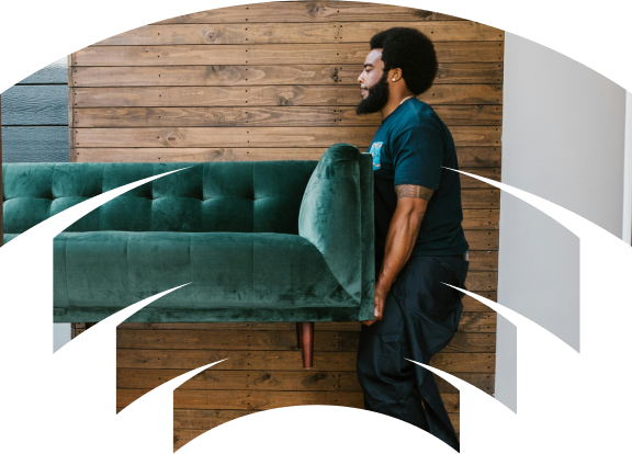A man carrying a large, green velvet sofa while walking past a wooden wall