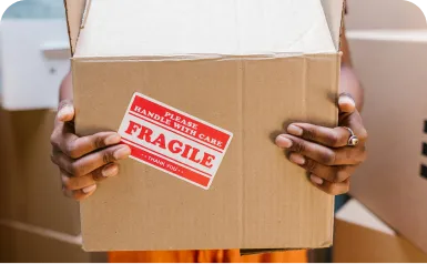 A person holding a box with a fragile sticker on it.