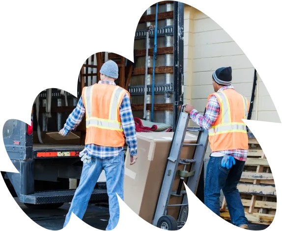 wo workers wearing safety vests and beanies unloading large boxes from a truck using a hand trolley
