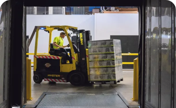 Warehouse worker operating a forklift, moving a pallet of stacked boxes