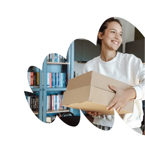 Smiling woman holding two cardboard boxes in a room with a bookshelf in the background