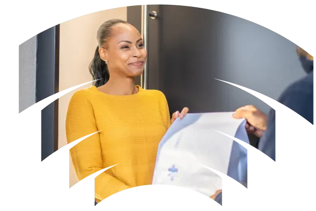 Smiling woman in a yellow sweater receiving a package from a delivery person at her door